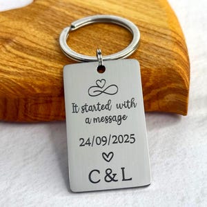 May include: A rectangular silver-toned metal keyring featuring an engraved infinity symbol with a heart, the text "It started with a message", the date "24/09/2025", a small heart icon, and the initials "C & L" centred on the front surface.