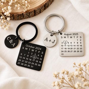 May include: Two metal keychains with square calendar charms and round initial tags. One set is black with October 2024 and C&A, the other is silver with August 2025 and A+J. Each calendar charm features a heart around a specific date.