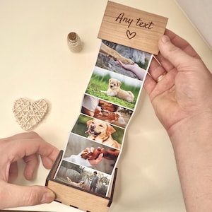 May include: A wooden photo box containing a strip of photos of dogs. The top of the box is engraved with the words "Any text" and a heart symbol. A small glass bottle with a cork and a woven heart are also visible.