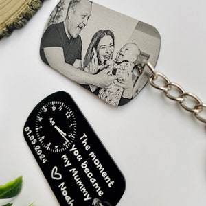 Puede incluir: Dos llaveros. Un llavero rectangular con una foto en blanco y negro de una familia. El otro es negro con un dise&ntilde;o de reloj y el texto "The moment you became my Mummy Noah".