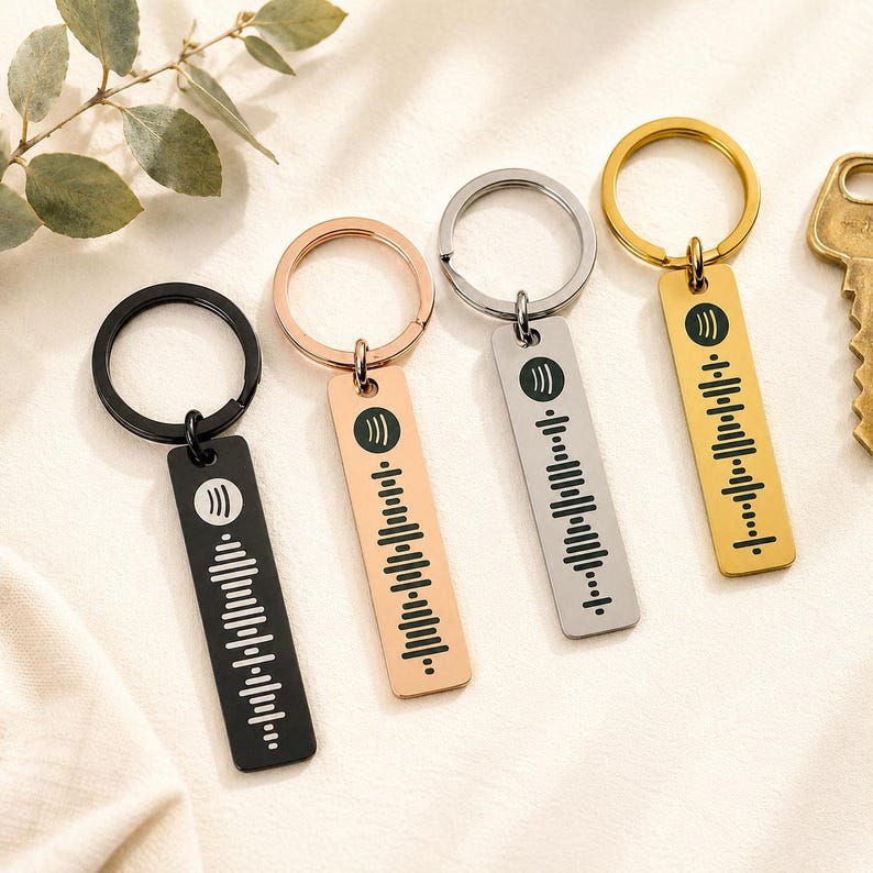 Op de afbeelding: Vier sleutelhangers met rechthoekige labels met een Spotify-code-ontwerp. De sleutelhangers zijn in de kleuren zwart, ros&eacute;goud, zilver en goud. Elk label heeft een cirkelvormig Spotify-logo en een reeks verticale lijnen.