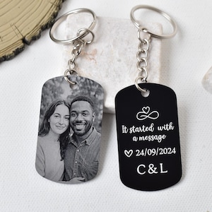 Op de afbeelding: Twee gepersonaliseerde sleutelhangers. Eén sleutelhanger heeft een zwart-witfoto van een stel. De andere is zwart met de tekst "It started with a message" en de datum 24/09/2024, plus initialen. Beide hebben zilveren sleutelringen.