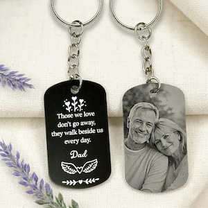May include: Two keyrings with silver chains. One black tag has the text "Those we love don't go away, they walk beside us every day. Dad." The other tag displays a black and white photo of a smiling couple.