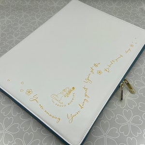 May include: White faux leather portfolio with a blue zip and gold zip pull. The portfolio features gold text that reads "You are amazing", "You're doing great", and "Be kind to yourself always". The Proud Midwife logo is also in gold.