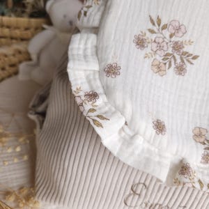 May include: A beige corduroy bag featuring a white muslin flap with a ruffled edge and a delicate floral print in shades of pink and brown. The name Esm&eacute;e is embroidered in cursive script on the lower beige corduroy section of the bag.