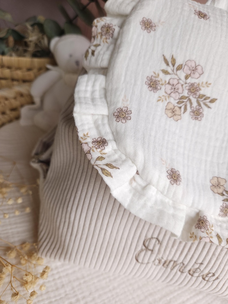 May include: A beige corduroy bag featuring a white muslin flap with a ruffled edge and a delicate floral print in shades of pink and brown. The name Esm&eacute;e is embroidered in cursive script on the lower beige corduroy section of the bag.