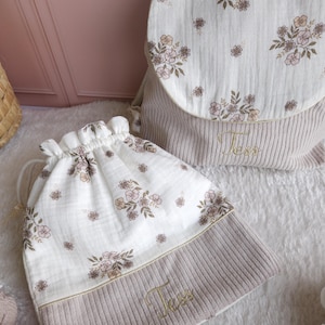 May include: A beige corduroy backpack and a matching drawstring bag, both featuring a white muslin fabric top with a delicate brown and pink floral print. Each item is embroidered with the name Tess in gold thread on the corduroy section.