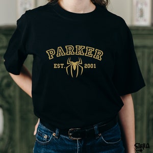 May include: Black t-shirt with a gold spider graphic and the text "PARKER EST. 2001" printed on the front.