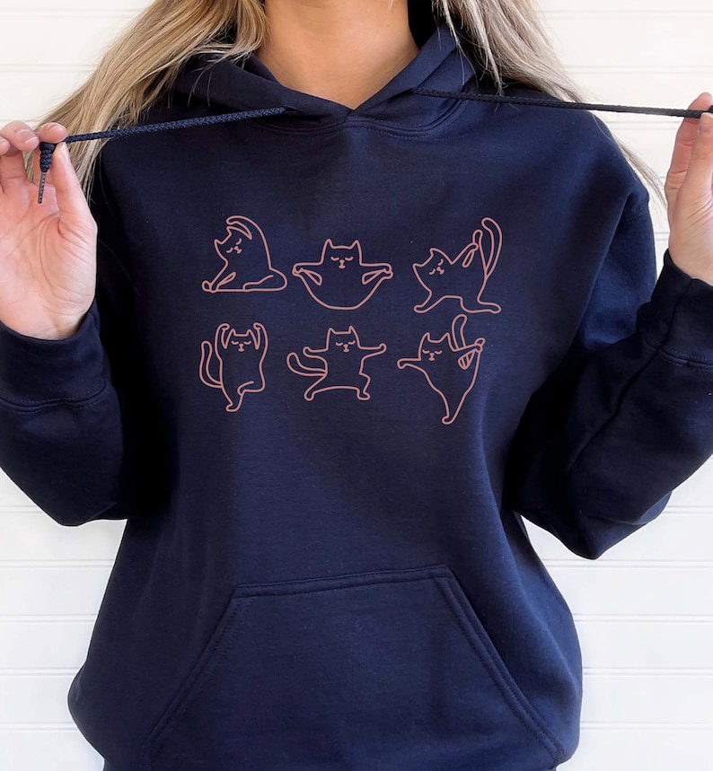 May include: A black hoodie with a pink outline of cats doing yoga poses. The hoodie has a drawstring hood and a kangaroo pocket.
