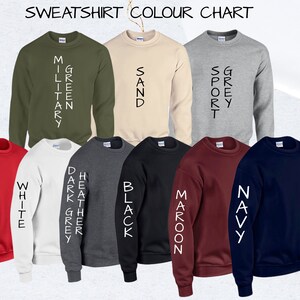 May include: A color chart of sweatshirts in various colors, including red, white, dark grey, heather grey, black, maroon, navy, sand, military green, and sport grey. The color names are printed vertically on the sleeves of each sweatshirt.