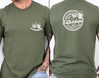 May include: Olive green t-shirt with a white graphic on the front featuring a skeleton hand giving the middle finger and a beer mug, with the word "FATHERHOOD". The back of the shirt has a circular design with the text "Surviving Fatherhood One Beer at a Time".