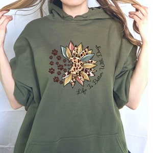 May include: A green hooded sweatshirt with a graphic of a sunflower with paw prints and the text "Life Is Better With Dogs".