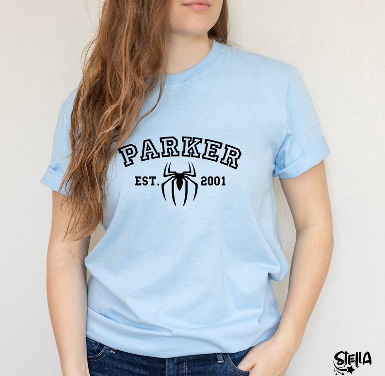 May include: Light blue t-shirt with black text that reads "Parker Est. 2001" and a black spider graphic.