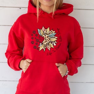 May include: Red hooded sweatshirt with a sunflower design featuring a leopard print and paw prints. The text "Life Is Better With Dogs" is printed on the sweatshirt.