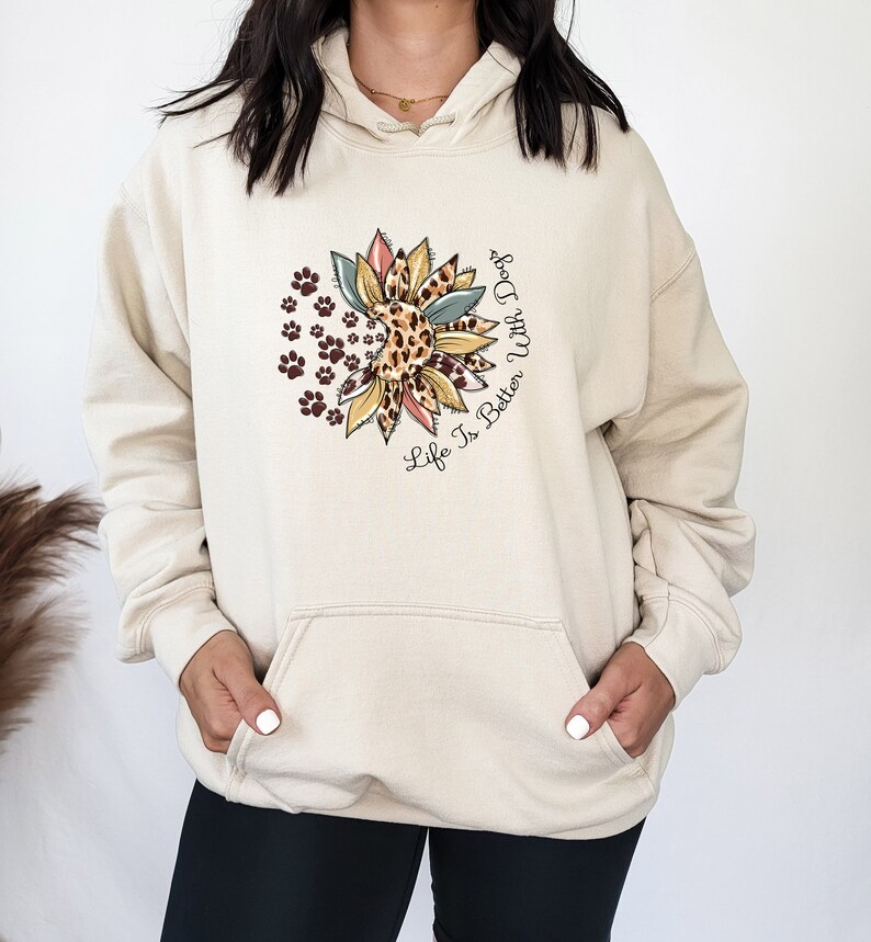 May include: A cream-colored hoodie with a graphic of a sunflower with paw prints and the text "Life Is Better With Dogs".