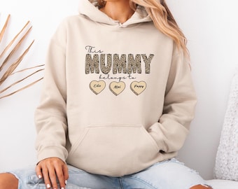 May include: A beige hoodie with a leopard print design that says "This Mummy belongs to" with three hearts that say "Edie", "Mai", and "Poppy".