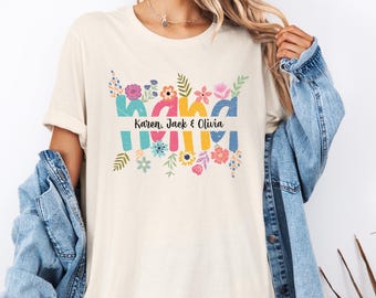 Puede incluir: Camiseta color crema con la palabra "Mama" en letras coloridas y decoradas con flores. Los nombres "Karen, Jack & Olivia" están impresos debajo de la palabra "Mama". La camiseta tiene un corte casual y relajado.