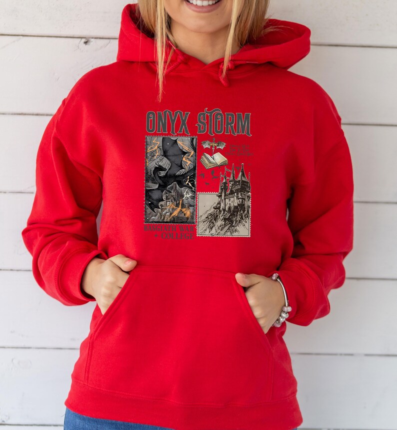 Peut inclure: Sweat-shirt &agrave; capuche rouge avec un imprim&eacute; graphique d'un ch&acirc;teau, d'un livre et d'une chauve-souris avec le texte "ONYX STORM" et "Something Wicked This Way Comes".
