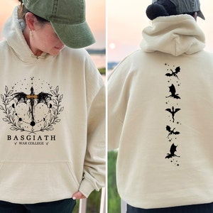 May include: A cream coloured hoodie with a black dragon graphic on the front and five black dragons on the back. The front graphic includes the text "BASGIATH WAR COLLEGE".