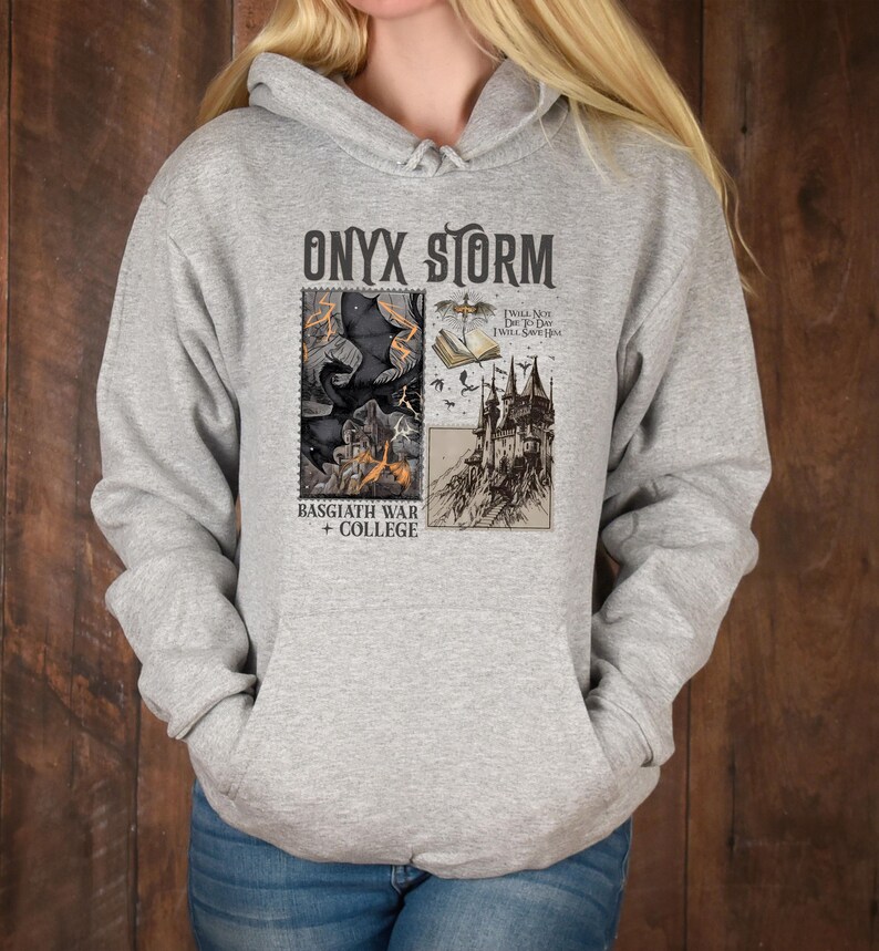 Peut inclure: Un sweat &agrave; capuche gris avec un imprim&eacute; graphique noir et blanc d'un ch&acirc;teau, d'un livre et d'un dragon. Le texte "ONYX STORM" est imprim&eacute; en noir en haut du graphique. Le texte "BASGIATH WAR + COLLEGE" est imprim&eacute; en noir en bas du graphique.