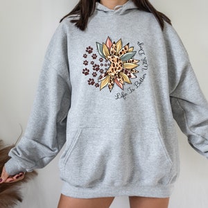 May include: Gray hooded sweatshirt with a sunflower design featuring a leopard print and paw prints. The text "Life Is Better With Dogs" is printed on the sweatshirt.