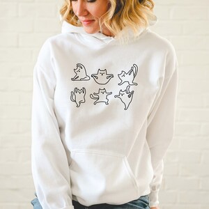 May include: White hooded sweatshirt with a black outline graphic of cats doing yoga poses.