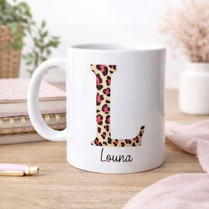 Peut inclure: Tasse en céramique blanche avec un grand "L" à imprimé léopard et des accents roses. Le nom "Louna" est imprimé en dessous en script noir. La tasse a une anse incurvée.