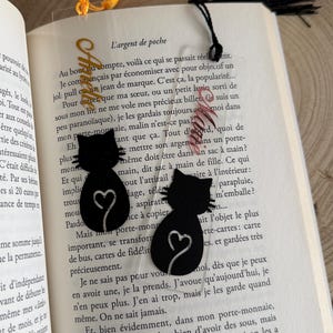 Peut inclure: Deux marque-pages en forme de chat noir avec un cœur sur la queue. Les marque-pages sont en acrylique transparent et ont un pompon doré.