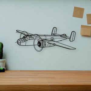 May include: Black metal wall art depicting a detailed outline of a vintage airplane. The artwork is mounted on a white wall above a wooden desk. A camera, books, and a cactus are on the desk.