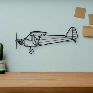 Könnte beinhalten: Schwarze Draht-Wanddekoration eines Doppeldeckers an einer weißen Wand. Auf einem Holzschreibtisch befinden sich Bücher, eine Kamera, ein Kaktus und eine Holzfigur. Eine dekorative Szene.