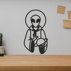 May include: Black and white line art illustration of an alien holding a planet. The alien is wearing a robe and has a halo. The illustration is on a white wall.