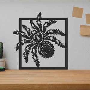 Puede incluir: Ilustración en blanco y negro de una araña en un marco cuadrado. La araña tiene ocho patas y está mirando hacia el lado derecho de la imagen.