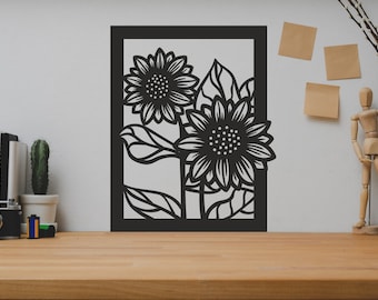 May include: Black and white wall art featuring a cutout design of two sunflowers with leaves. The art is framed in a black frame and is hanging on a white wall.