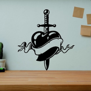 May include: Black and white wall decal of a heart pierced by a sword with a banner wrapped around the heart.