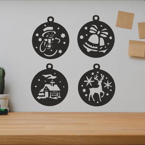 Könnte beinhalten: Vier schwarze und weiße Weihnachtsbaumschmuck-Schablonen mit verschiedenen Designs: ein Schneemann, eine Glocke, ein Haus und ein Rentier. Die Schablonen befinden sich an einer weißen Wand.