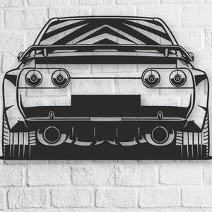 Könnte beinhalten: Schwarze Metall-Wandkunst eines Sportwagen-Hecks, montiert an einer weißen Backsteinmauer. Das Kunstwerk zeigt detaillierte Ausschnitte der Rücklichter, Auspuffrohre und des Spoilers. Ein schlankes, modernes Design für Autoliebhaber.
