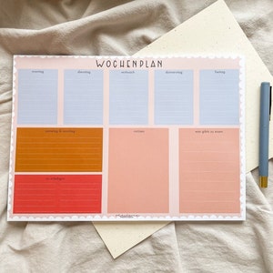 Könnte beinhalten: Ein Wochenplaner mit rosa Hintergrund und einem gewellten Rand. Der Planer hat Abschnitte für jeden Tag der Woche, mit Platz zum Aufschreiben von Aufgaben, Notizen und Mahlzeiten. Der Planer hat auch einen Abschnitt zum Aufschreiben von Dingen, an die man sich erinnern soll.