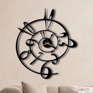 May include: A black metal wall clock with a unique spiral design. The clock features stylized numbers and hands, with a gold-colored center. The clock is mounted on a beige wall above a beige sofa, creating a modern aesthetic.