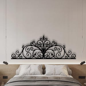 Peut inclure: Une décoration murale en métal noir présentant un motif complexe et symétrique de volutes avec des ornements élaborés et une pointe centrale. Cet élément décoratif est fixé horizontalement sur un mur au-dessus d'un cadre de lit.