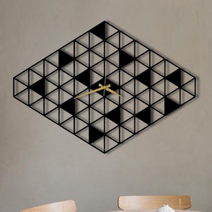 May include: A black and white geometric wall clock with gold hands. The clock is in the shape of a diamond and is hanging on a light gray wall.