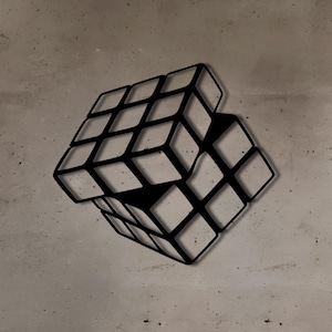 Peut inclure: Une sculpture murale en métal noir représentant un cube de Rubik, le cube semblant flotter dans les airs contre un mur en béton.