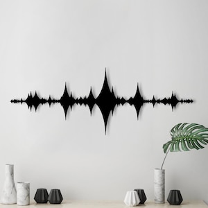 Può includere: Arte da parete in metallo nero a forma di onda sonora. L'opera d'arte è montata su una parete bianca ed è circondata da oggetti decorativi.