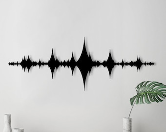 May include: Black metal wall art in the shape of a sound wave. The art is mounted on a white wall and is surrounded by decorative objects.