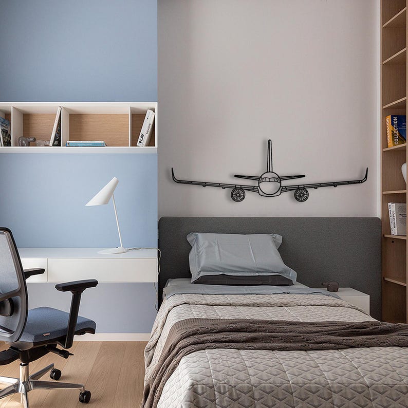 May include: A modern bedroom with a blue and white color scheme. A black metal airplane wall decoration is above a bed with gray bedding and a brown blanket. A white desk with a white lamp and a blue chair is in the corner.