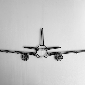 May include: Black metal airplane wall art. The artwork depicts a stylized airplane with wings, a fuselage, and two engines. The design is a minimalist outline, suitable for aviation enthusiasts or modern decor.