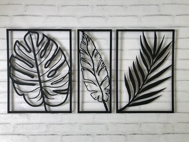 Puede incluir: Tres piezas de decoraci&oacute;n de pared de metal negro con dise&ntilde;os recortados de hojas tropicales. Las hojas son de estilo minimalista y est&aacute;n enmarcadas en metal negro.