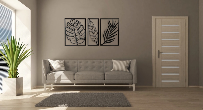 Puede incluir: Un interior de sala de estar con un sof&aacute; gris, una planta en maceta y tres piezas de arte de pared enmarcadas en negro con siluetas de hojas tropicales.