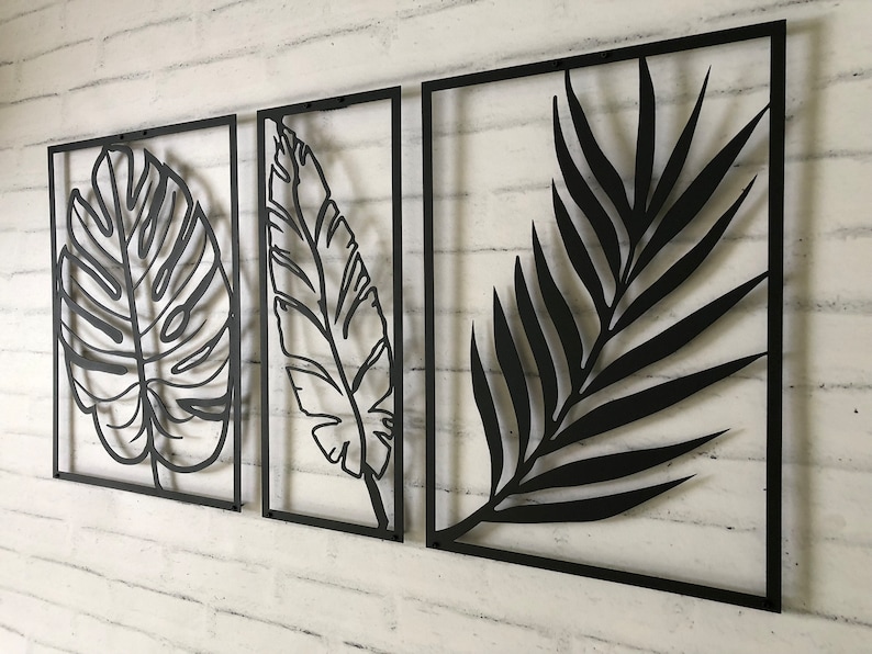 Puede incluir: Tres piezas de decoraci&oacute;n de pared de metal negro con dise&ntilde;os recortados de hojas tropicales. Las hojas son de estilo minimalista y est&aacute;n dispuestas en fila.