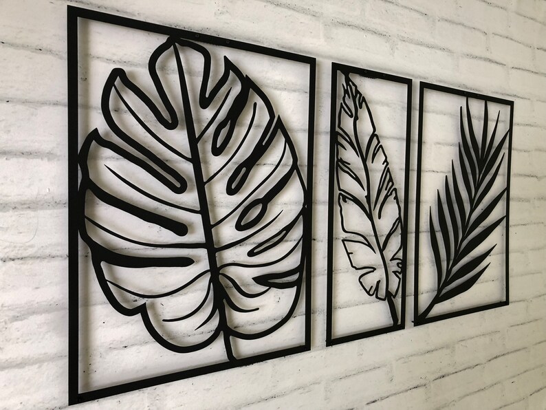 Puede incluir: Tres piezas de decoraci&oacute;n de pared de metal negro con dise&ntilde;os recortados de hojas tropicales. Las piezas son rectangulares y tienen un estilo simple y moderno.