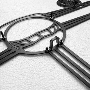May include: Black metal wall art featuring a stylized lacrosse stick and ball design. The piece has a circular element and several straight, parallel lines, with visible mounting hardware.